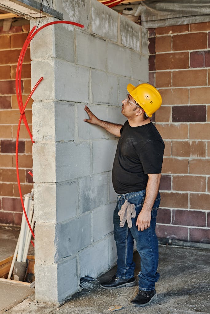 Construction worker with hard hat inspects brick wall in an indoor site.